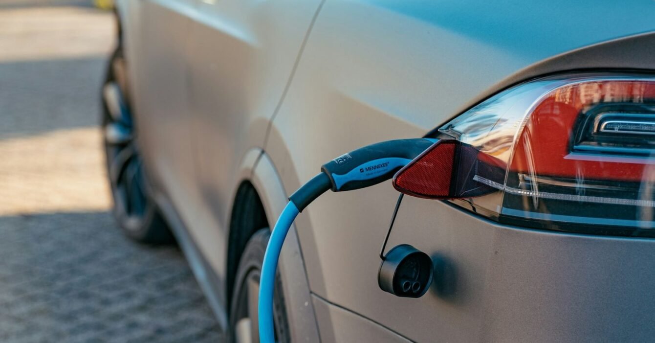 ernest-ojeh-UrCV-U9hhCo-unsplash Thailand EV market share 2025: An electric vehicle charging with a blue cable plugged into its rear socket, parked on a paved surface.