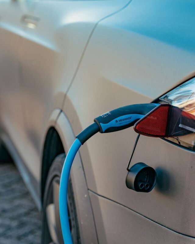 Thailand EV market share 2025: An electric vehicle charging with a blue cable plugged into its rear socket, parked on a paved surface.